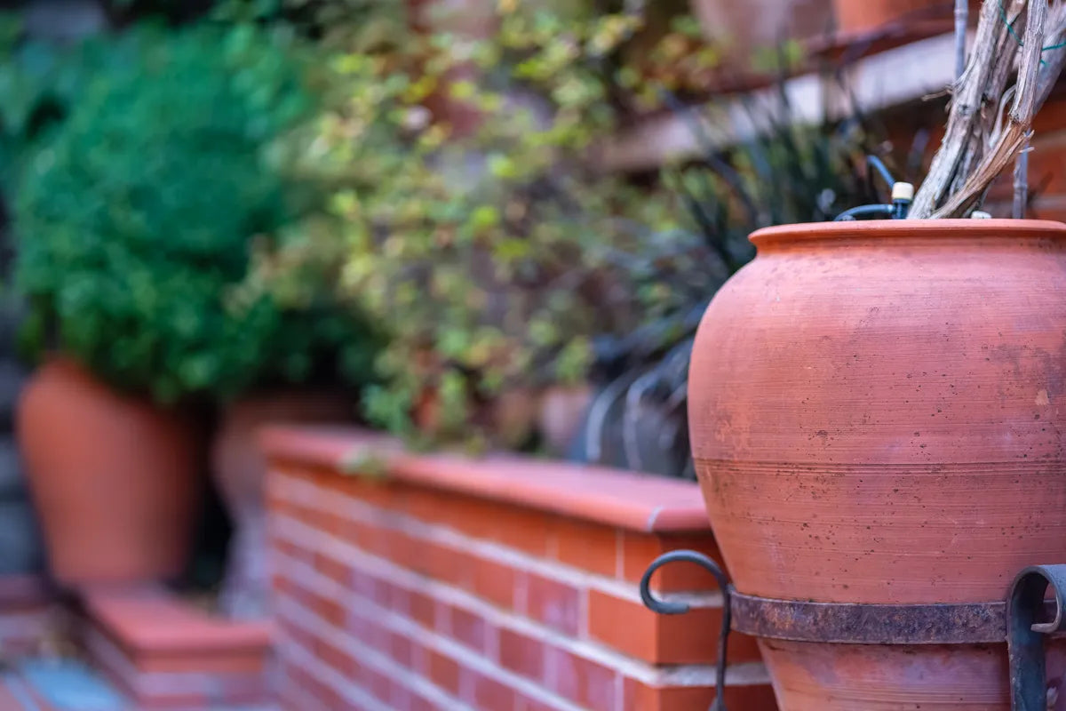 Großer Terracotta-Krug als Blickfang vor einer Backsteinmauer im bepflanzten Garten