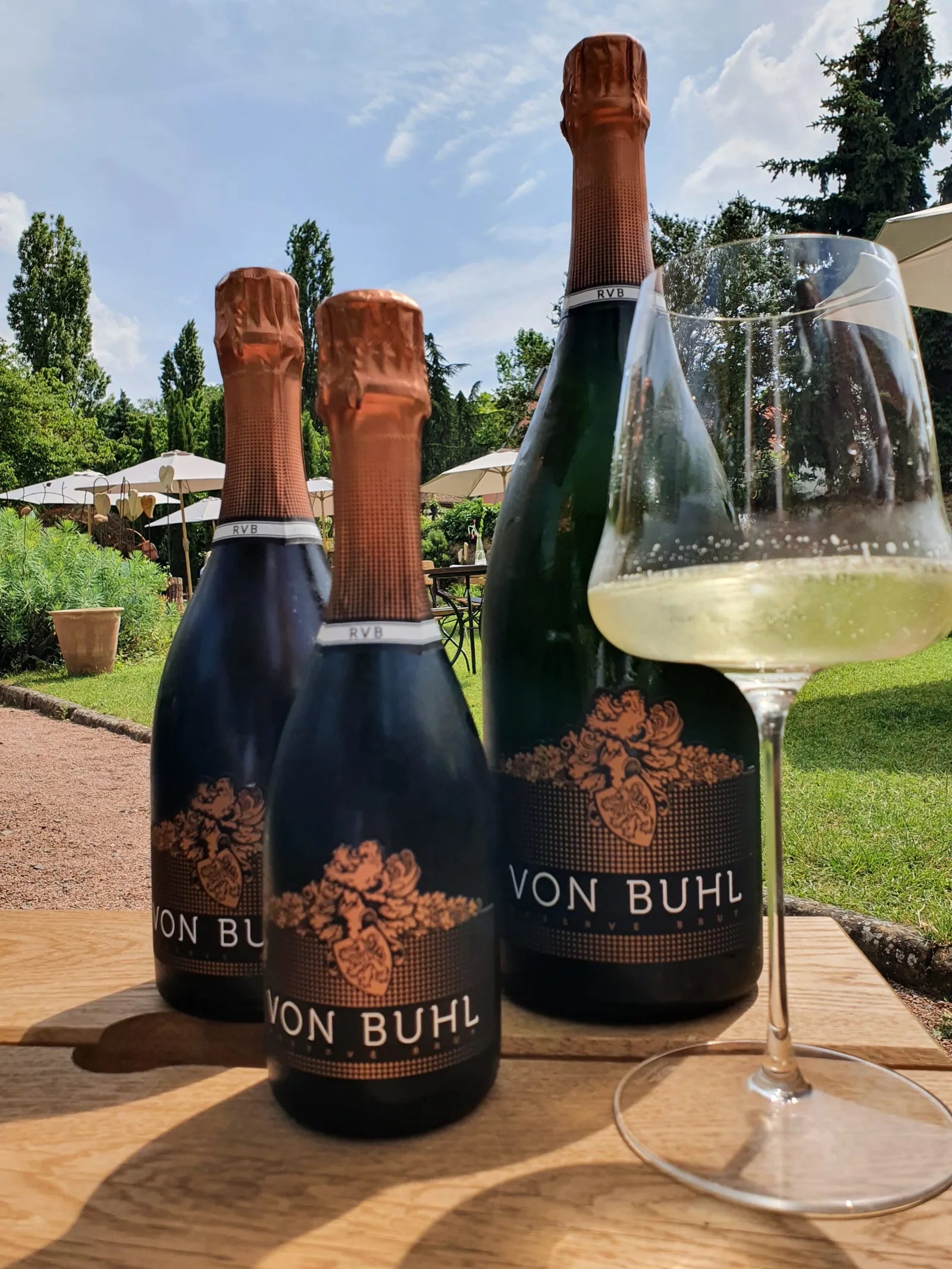 Sektflaschen und ein gefülltes Glas vor dem Garten der Weinbar