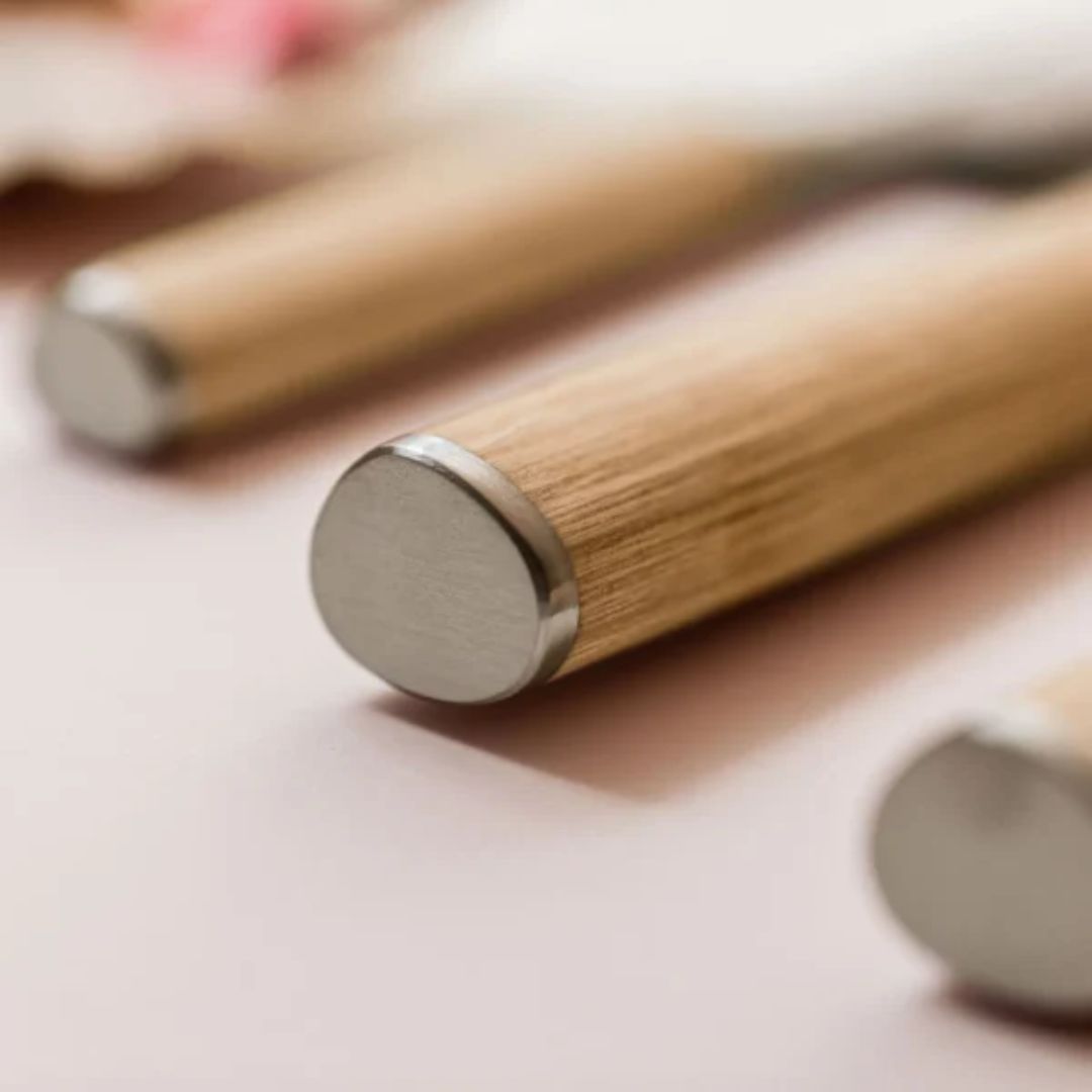 Nahaufnahme von Holzgriffen mit Metallkappen, möglicherweise mit dem Kai Shun Classic White DM-0705W Brotmesser 23,0 cm "THE MAGIC KAI WISHLIST", auf einer zartrosa Oberfläche. Der Fokus liegt auf den abgerundeten Metallenden und der geringen Tiefenschärfe.