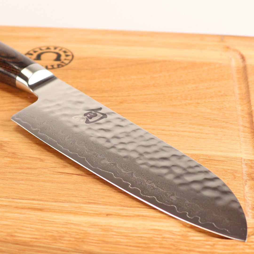 Das Kai Shun Premier Tim Mälzer TDM-1727 kleines Santoku mit einer 14 cm langen Klinge mit Damaszenermuster ruht auf dem mitgelieferten 30x20 cm großen Schneidebrett.